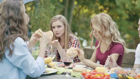 Amigos-comiendo-hamburguesas-en-la-mesa-en-la-fiesta-al-aire-libre