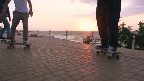 Group-of-young-people-skateboarding-on-the-road-in-the-early-morning-near-the-sea,-close-up-shot