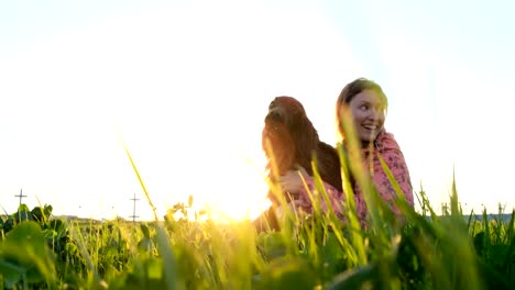 Mujer-abrazando-al-perro-al-atardecer-y-riendo,-niña-con-mascota-sentados-sobre-la-hierba-y-descansar-en-la-naturaleza