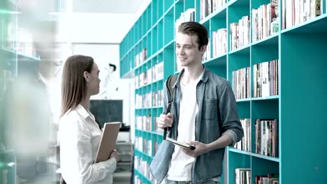 Two-students,-boy-and-girl,-having-friendly-talk-in-university-library,-textbooks-in-their-hands