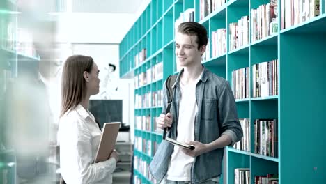 Zwei-Studenten,-jungen-und-Mädchen,-mit-freundlichen-Gespräch-in-Universitätsbibliothek,-Lehrbücher-in-ihren-Händen