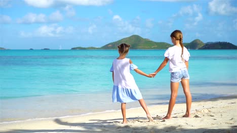 Little-happy-funny-girls-have-a-lot-of-fun-at-tropical-beach-playing-together.-Sunny-day-with-rain-in-the-sea