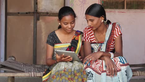 Bis-auf-zwei-Damen-arbeiten-und-diskutieren-wichtige-Arbeit-auf-einem-Tablet-mit-Touchscreen-im-Komfort-ihres-Hauses-in-einer-kleinen-Stadt-in-Rajasthan,-Indien-tragen-lokale-Kleider-Make-up-und-Kleidung