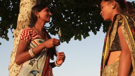 Handheld-stabilized-shot-two-females-girls-sharing-secrets-and-joking-kidding-fun-gossip-freedom-independent-outdoor-tree-park-public-alone-secrets-hidden-casual-friends-buddy-sari-India-Rajasthan