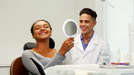 Hermosa-mujer-comprobando-su-sonrisa-en-el-espejo-en-la-clínica-dental