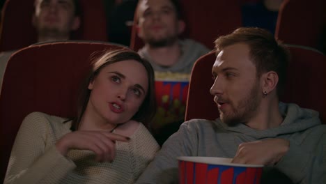 Young-couple-enjoying-film-in-cinema.-Couple-eating-popcorn-and-discussing-movie