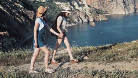 Two-friends-hiker-woman-walking-on-path-holding-hands-enjoying-amazing-mountain-seascape