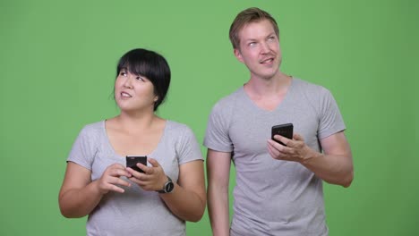 Young-happy-multi-ethnic-couple-using-phone-and-thinking-together