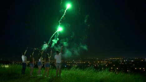 The-five-people-hold-a-firework-sticks-on-the-city-lights-background.-night-time