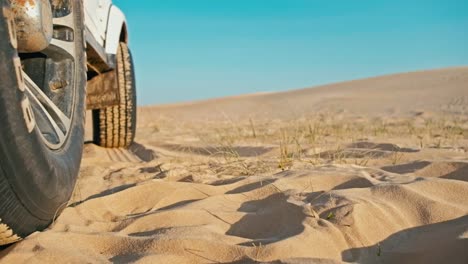 Closeup-de-las-piernas-de-una-mujer-joven-junto-a-un-vehículo-4-x-4-disfrutando-del-atardecer-en-uno-de-la-duna-de-arena-desierto