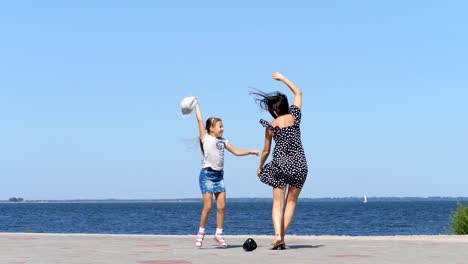 on-beach-mom-and-daughter,-beautiful-brunette-in-sundress-and-girl-child-teenager,-dancing,-listening-to-music-with-mini-music-bluetooth-portable-loudspeaker-on-a-hot-summer-day