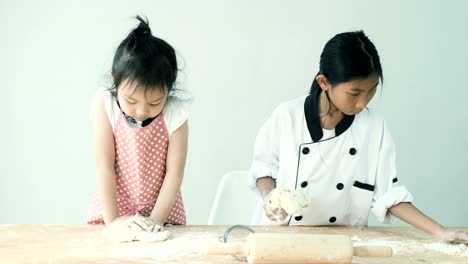 Happy-Asian-girls-with-pink-apron-and-chef-uniform-are-preparing-flour-for-cookie-or-pizza-dough,-slow-motion