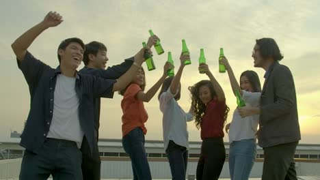 Group-of-young-friends-dancing-and-having-fun-celebrate-with-toast-and-clinking-raising-glasses-at-summer-rooftop-party-with-sunset-back-ground.-Slow-Motion.