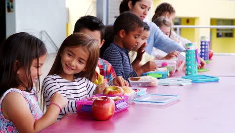 Escuela-primaria-los-niños-sentados-en-mesa-con-almuerzos