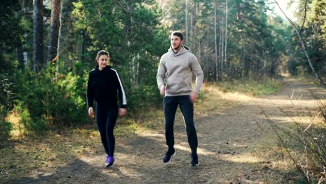 Happy-couple-young-woman-and-her-husband-are-doing-sports-in-park-jumping-on-the-ground-and-smiling.-Active-lifestyle,-modern-youth-and-nature-concept.