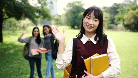 Three-female-women-students-waving-hands-in-the-park-while-focus-is-on-Asian-woman-in-the-front