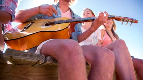 Mann-spielt-Gitarre-für-Freunde-auf-einen-Steg-im-Freien