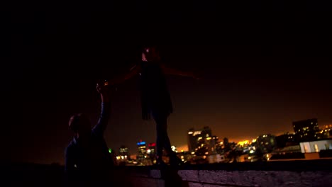 Man-is-holding-hand-with-girlfriend-who-is-balancing-on-rooftop-edge