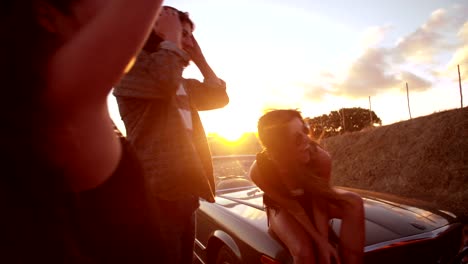 Teenage-boho-friends-sitting-on-a-convertible-hood-at-sunset