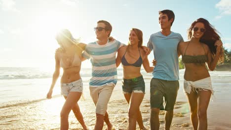 Group-of-friends-having-fun-walking-down-the-beach-at-sunset