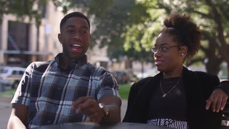 African-American-couple-at-an-outdoor-table-talking-and-laughing-together,-with-bokeh