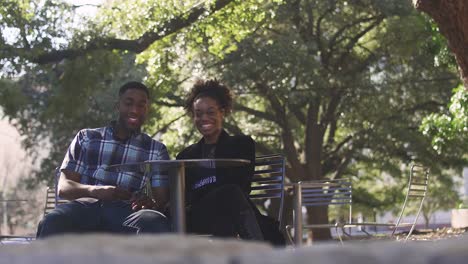 African-American-couple-at-an-outdoor-table-smiling-for-the-camera,-then-laughing,-bokeh