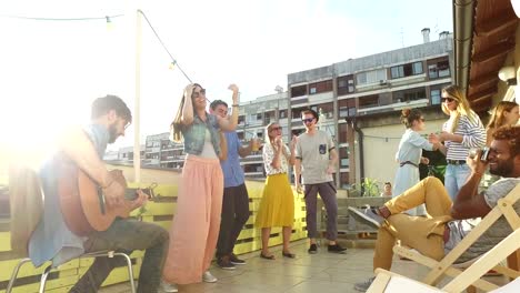 Musician-playing-guitar-at-rooftop-party,-people-dancing-and-taking-photos