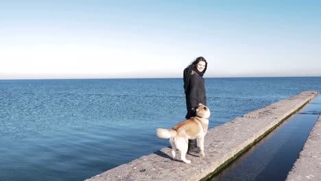 Young-woman-walking-in-lights-of-sun-with-siberian-husky-on-sea-pier