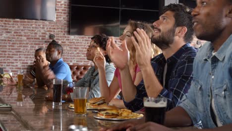 Group-Of-Friends-Watching-Game-In-Sports-Bar-On-Screens