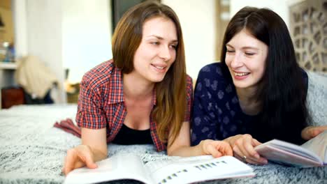 Two-young-woman-friends-are-watching-magazine-on-bed-in-bedroom-at-home