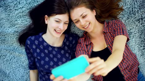 Top-view-of-two-pretty-girls-in-pajamas-making-selfie-portrait-on-bed-in-bedroom-at-home