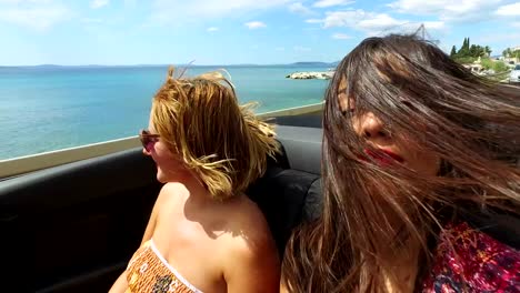 Two-attractive-women-riding-in-the-windy-back-seat-of-convertible