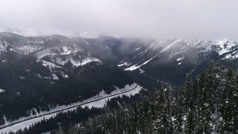 Winter-Roadtrip-Aerial-of-Travelers-on-Epic-Highway-in-Snowy-Mountain-Forest