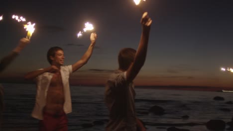 Grupo-de-jóvenes-felices-con-brillantes-fuegos-artificiales-en-las-manos-se-ejecutan-en-la-playa