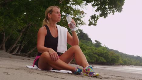 Woman-resting-and-drinking-water-after-run.