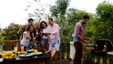 Junge-Leute-reden-mit-Smart-Handys-während-Latein-Mann-Kochen-Barbecue-Freundesgruppe-fröhlich-tanzen-treffen-auf-Sommerterrasse