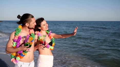 beach-panorama,-lovers-guy-and-girl-walking-With-cocktails,-happy-friends-in-hawaiian-Lei-Hug-and-have-fun-during-summer-Rest