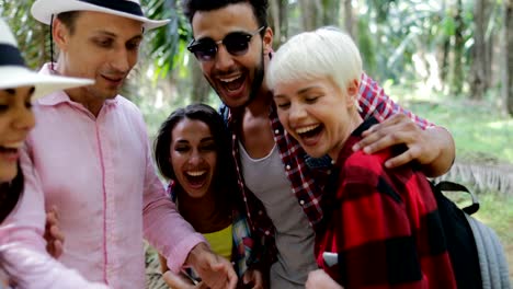 People-Group-With-Backpacks-Talking-Using-Cell-Smart-Phones,-Men-And-Woman-Watch-Photos-On-Trekking-In-Tropical-Palm-Tree-Forest