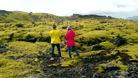 Aerial-view-of-two-woman-standing-on-the-lava-field-in-Iceland-and-enjoying-the-landscape.-Tourists-after-hiking