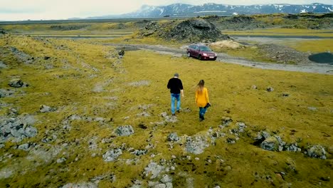 Aerial-back-view-of-young-couple-walking-through-volcanic-lava-field.-Stylish-man-and-woman-traveling-by-car-together