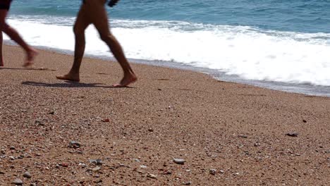 Fondo-de-vacaciones-de-verano-con-dos-jóvenes-caminando-por-la-playa-mientras-las-olas-del-mar-rompiendo-en-la-playa-de-arena-detrás-de-ellos