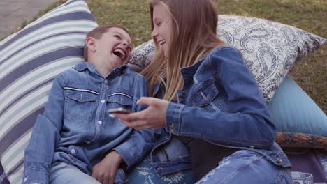 Sister-and-brother-laughing-and-sharing-a-joke-on-their-phone-and-having-fun-in-a-park