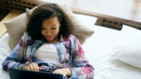 Cheerful-mixed-race-girl-having-video-chat-with-friends-using-laptop-camera-while-lying-on-bed