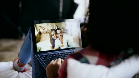 Curly-young-woman-having-video-chat-with-friends-using-laptop-camera-while-lying-on-bed