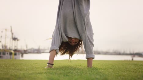 Young-girl-is-doing-a-handstand-and-smiles-into-the-camera-in-front-of-a-beautiful-harbour-background