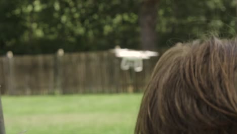 Young-little-girl-flying-a-drone-playing-outdoor-on-summer-in-green-grass-field-remote-pilot-slow-motion