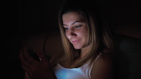 Woman-In-Dark-Using-Smartphone-Before-Bedtime,-Face-Illuminated-From-Screen