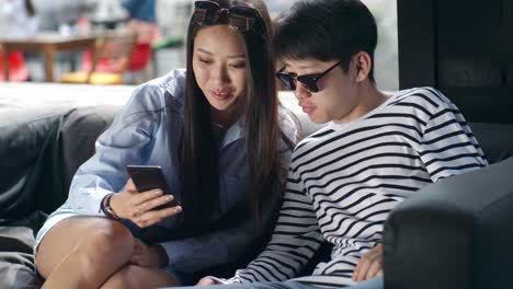 Young-Asian-Couple-Watching-Video-on-Smartphone-in-Outdoor-Cafe