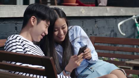 Asian-Teenage-Couple-Using-Smartphone-and-Laughing-Outdoors