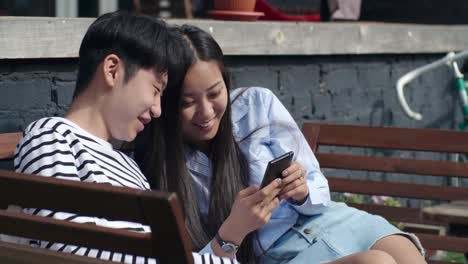 Asiatische-Teenager-Paar-mit-Smartphone-und-Lachen-im-freien